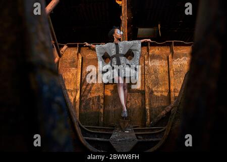 Frau trägt Kleid und sitzt auf rostigen Schiff Wrack Stockfoto