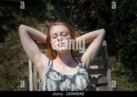 Portrait einer jungen Frau, die auf dem Liegestuhl im Garten sonnenbaden Stockfoto