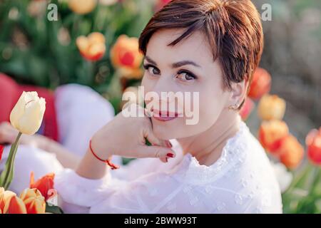 Porträt einer lächelnden Frau, die im Tulpenfeld sitzt Stockfoto