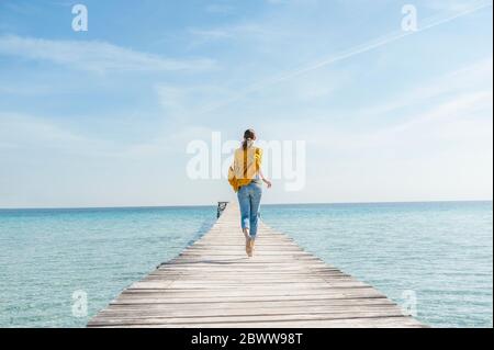 Rückansicht einer Frau, die barfuß auf dem Steg läuft, Mallorca, Spanien Stockfoto