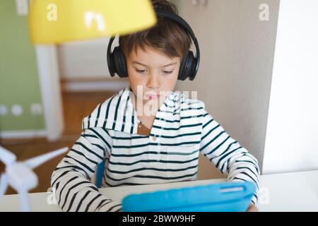 Junge tun Heimschooling und mit Tablet und Kopfhörer zu Hause Stockfoto