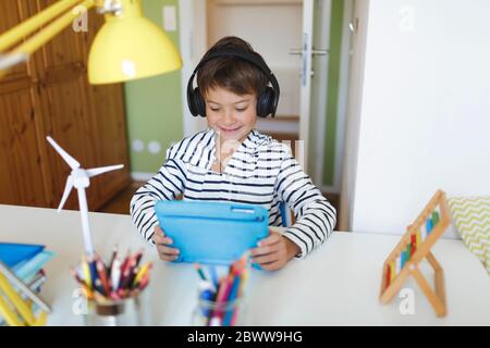 Junge tun Heimschooling und mit Tablet und Kopfhörer zu Hause Stockfoto