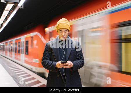 Stilvoller Mann mit Smartphone und Ohrhörer in der U-Bahn-Station Stockfoto