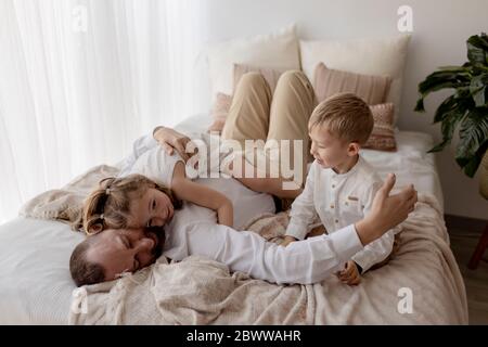 Vater liegt auf dem Bett und kuschelt mit seinen beiden Kindern Stockfoto