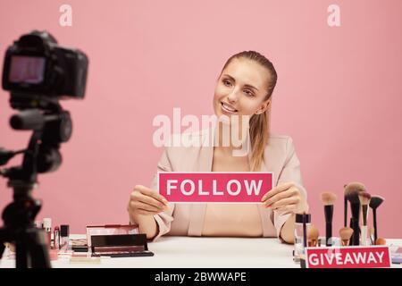 Junge Frau lächelt vor der Kamera und sagt zu ihren Anhängern, ihrem Beauty-Blog zu folgen Stockfoto