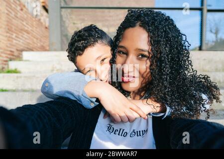 Portrait von glücklicher Mutter und Sohn sitzen zusammen auf Schritten Selfie machen Stockfoto