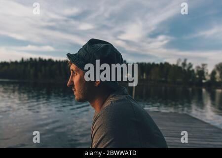 Junger Mann mit Hut, der auf den See schaut Stockfoto