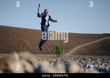 Aufgeregt Geschäftsmann auf einem stillgerades Bergwerk Spitze Springen neben Pflanze Stockfoto