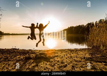 Freunde springen in der Luft am Seeufer gegen den Himmel während des Sonnenuntergangs Stockfoto