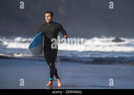Behinderter Surfer mit Surfbrett am Strand Stockfoto