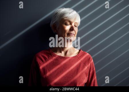 Porträt einer älteren Frau mit geschlossenen Augen, die sich an der Wand lehnt Stockfoto