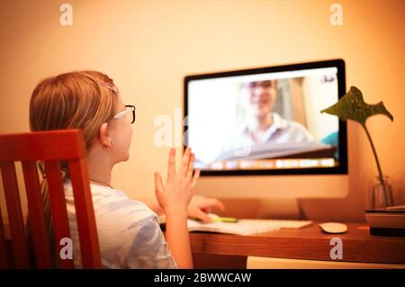 Rückansicht des anonymen Mädchens, das den Arm hebt, während es am Schreibtisch sitzt und zu Hause Online-Unterricht besucht Stockfoto