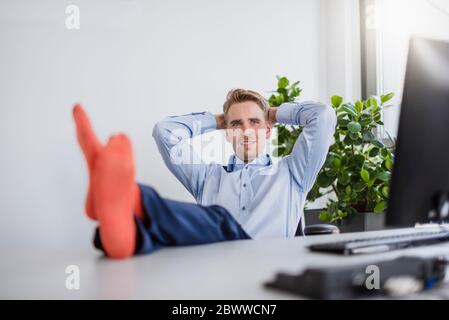 Lächelnder Geschäftsmann, der im Büro sitzt und die Füße auf dem Schreibtisch hat Stockfoto