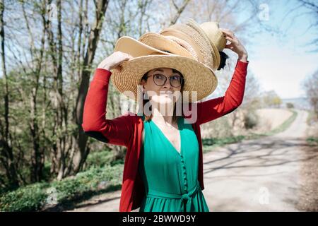 Portrait einer reifen Frau mit einem Stapel Strohhüte auf ihrem Kopf im Freien Stockfoto