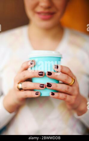 Ernte anonyme Frau in warmen Pullover mit dunkler Maniküre hält Einweg Tasse Kaffee während der Ruhepause am Holztisch Stockfoto