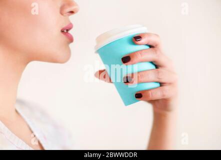 Ernte anonyme Frau in warmen Pullover mit dunkler Maniküre hält Einweg Tasse Kaffee während der Ruhepause am Holztisch Stockfoto