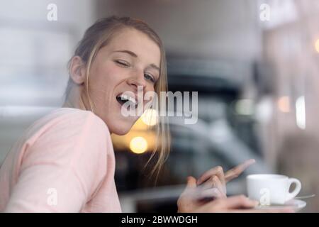 Porträt einer jungen Frau, die hinter einem Fensterscheibe in einem Café Grimassen Stockfoto