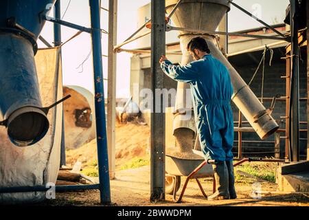 Junger Bauer trägt blauen Gesamtlader aus einem Silo in Schubkarre Stockfoto