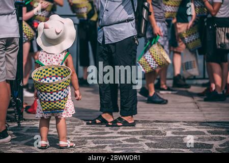 Yangshuo, China - August 2019 : nettes kleines chinesisches Mädchen trägt großen Weidenkorb auf dem Rücken, während Sie auf einer Straße und Einkaufen mit ihren Eltern Stockfoto