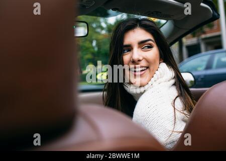 Lächelnde junge Frau, die im Auto über die Schulter schaut Stockfoto