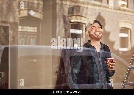 Mann, der die Lage des Ladens renoviert, Kaffee trinkt und aus dem Fenster schaut Stockfoto
