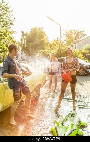 Drei Freunde waschen gelben Oldtimer im Sommer Spaß haben Stockfoto