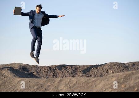 Reifer Geschäftsmann mit Laptop springen auf einem stillgerades Mine Tipp Stockfoto