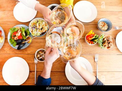 Gruppe von Ernte anonymen Freunden klirren Gläser mit Wein während der Versammlung um Tisch mit köstlichen Gerichten während des Hausdinner. Draufsicht Stockfoto