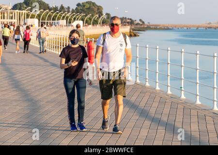 Huelva, Spanien - 23. Mai 2020: Menschen, die bei Sonnenuntergang an der Promenade von Huelva spazieren, während des Alarmzustandes und des Quarans schützende oder medizinische Gesichtsmasken tragen Stockfoto