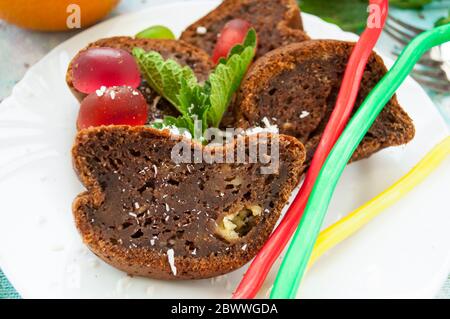 Stücke von Schokoladenkuchen und bunte Gelee Süßigkeiten mit Kokosflocken auf einem weißen Teller mit Minze Nahaufnahme verziert bestreut Stockfoto