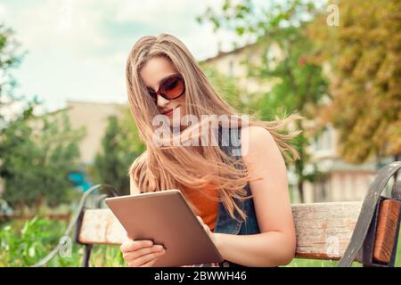 Arbeiten an der Bremsbeläge. Schöne Frau Blick auf digitale Tablette im Freien und lächelnd leichtes Lächeln. Gemischte Rasse asiatischen russischen Modell auf grünen Stadtbild backgr Stockfoto