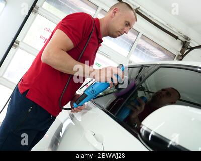 Ein professioneller Mitarbeiter für Karosserie- und Stirnlampenpolieren transportiert das Auto nach dem Lackieren oder der Vorbereitung auf den Verkauf. Konzept: Freshen Autos, Auto. Stockfoto