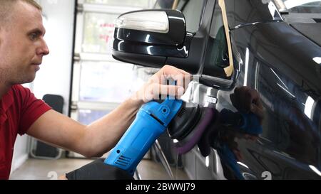 Ein professioneller Mitarbeiter für Karosserie- und Stirnlampenpolieren transportiert das Auto nach dem Lackieren oder der Vorbereitung auf den Verkauf. Konzept: Freshen Autos, Auto. Stockfoto