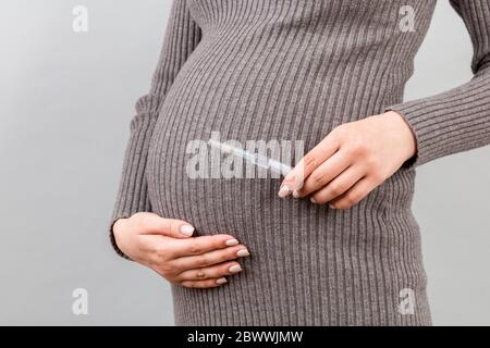 Nahaufnahme der Spritze für die Injektion in die Hand der schwangeren Frau auf farbenfrohem Hintergrund mit Kopierraum. Medizinische Behandlung während der Schwangerschaft Konzept. Stockfoto