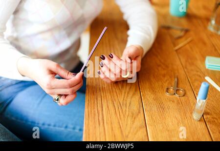 High-Winkel-Seitenansicht der Ernte anonyme Frau in Freizeitkleidung sitzen am Holztisch mit verschiedenen Werkzeugen für Maniküre und Polieren Nägel mit Nagel Stockfoto