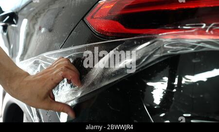 Nahaufnahme des PPF-Installationsprozesses an einem Scheinwerfer und einer Motorhaube. PPF ist eine Lackschutzfolie, die Farbe vor Kratzern und Steinschlag schützt. Stockfoto