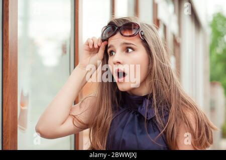 Wow, tolles Angebot. Überrascht junge Frau mit Sonnenbrille oben schauend schockiert durch das Geschäft Fenster an den Verkäufen. Stockfoto