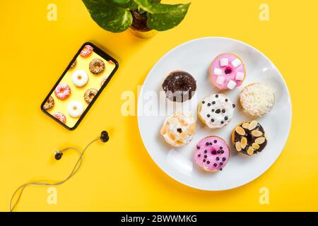 Bunte Donuts auf einem weißen Teller auf gelbem Hintergrund serviert. Stockfoto