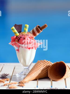 Nahaufnahme von Glas mit Erdbeereis auf Blur Bokeh Hintergrund mit Kopierraum. Himbeer-Sorbet mit Waffel-Schokolade-Zapfen auf weißer Tischplatte o Stockfoto