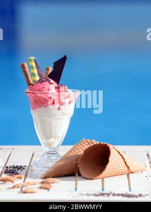 Nahaufnahme von Glas mit Vanille, Wassermelone Eis auf Unschärfe Bokeh Hintergrund mit Kopierraum. Kirschbeeren Sorbet mit Waffelzapfen und Schokolade pi Stockfoto
