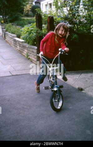 Ein 7-jähriges Mädchen, das ein rotes Top und Jeans trägt und mit ihrem Raleigh Tomahawk Fahrrad durch die Straßen der Londoner Vororte, Hatch End, Middlesex, Großbritannien, fährt Stockfoto