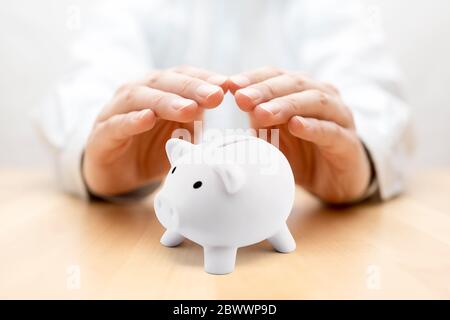 Schützen Sie Ihr Geld. Kleines Sparschwein mit Händen bedeckt Stockfoto