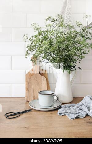 Rustikale Küche innen. Stillleben Komposition mit Tasse Kaffee, Holzhackbretter und Kuh Petersilie Bouquet in Krug. Weiße Ziegelmauer, Metro Stockfoto