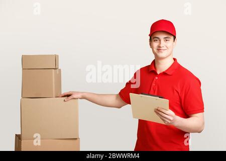 Paketkontrolle durch Postarbeiter. Lächelnder Kurier in Uniform hält ein Tablet für Notizen und legt seine Hand auf einen Karton Stockfoto