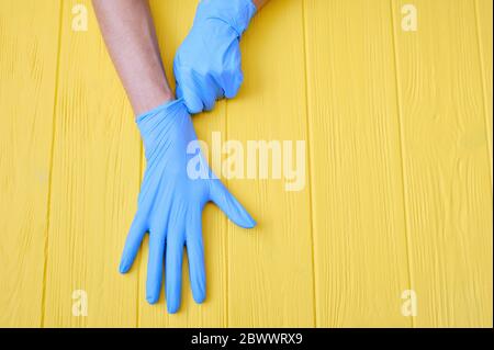 Blaue Nitrilhandschuhe. Hände eines Sanitäter in den blauen Latexhandschuhen auf gelbem Holzhintergrund mit Platz für deinen Text Stockfoto