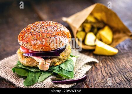 Vegetarischer Burger mit pommes im Hintergrund, Gourmet-Essen auf rustikalem Holztisch. Stockfoto