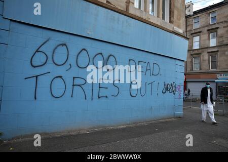 Eine Person passiert Graffiti im Zusammenhang mit dem Coronavirus in Glasgow, während Schottland in Phase eins des Plans der schottischen Regierung geht, die Sperre schrittweise zu heben. Stockfoto