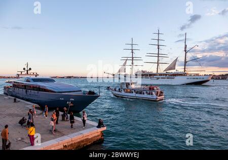 Drei Mast Segelschiff, MV Sea Cloud ll, verlassen Venedig unter einem warmen Sonnenuntergang glühen, im Gegensatz dazu ein Wasserbus und super Yacht im Vordergrund Stockfoto