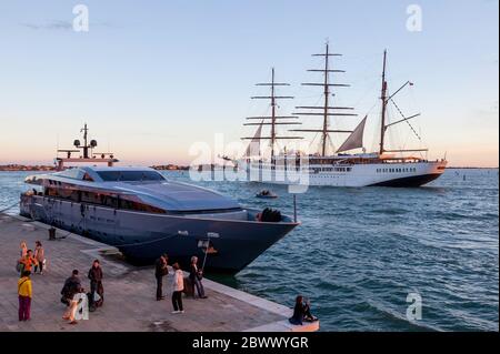 Drei Mast Segelschiff, MV Sea Cloud ll, verlassen Venedig, Italien, unter einem warmen Sonnenuntergang mit einer Superyacht im Vordergrund und Zuschauer vor Anker Stockfoto