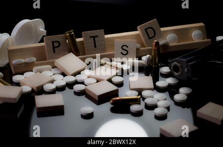 PTSD im Text mit Pillen, Kugeln und Handfeuerwaffe. Konzept der posttraumatischen Belastungsstörung mit geöffneter Flasche Antidepressiva, Munition und einer Hand Stockfoto